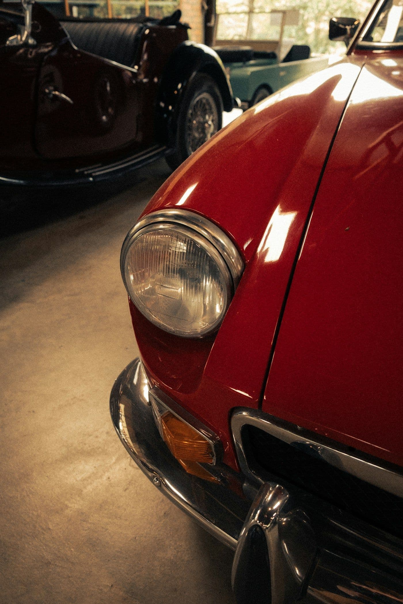 The headlight and fender of a red classic car on a garage floor
