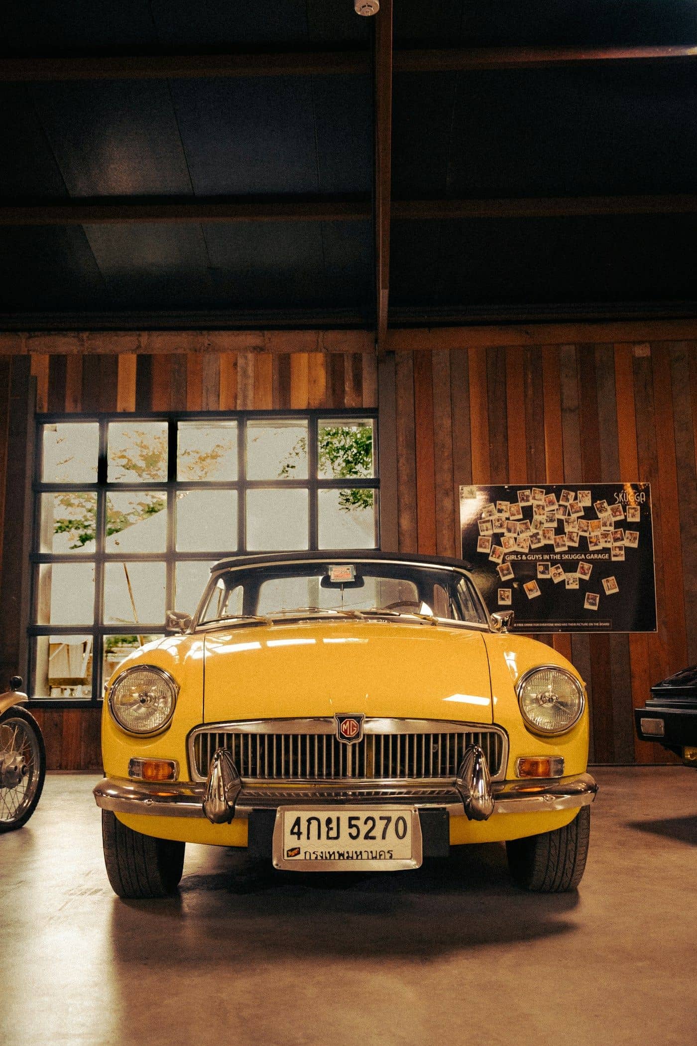 A yellow vintage convertible beneath timber trusses