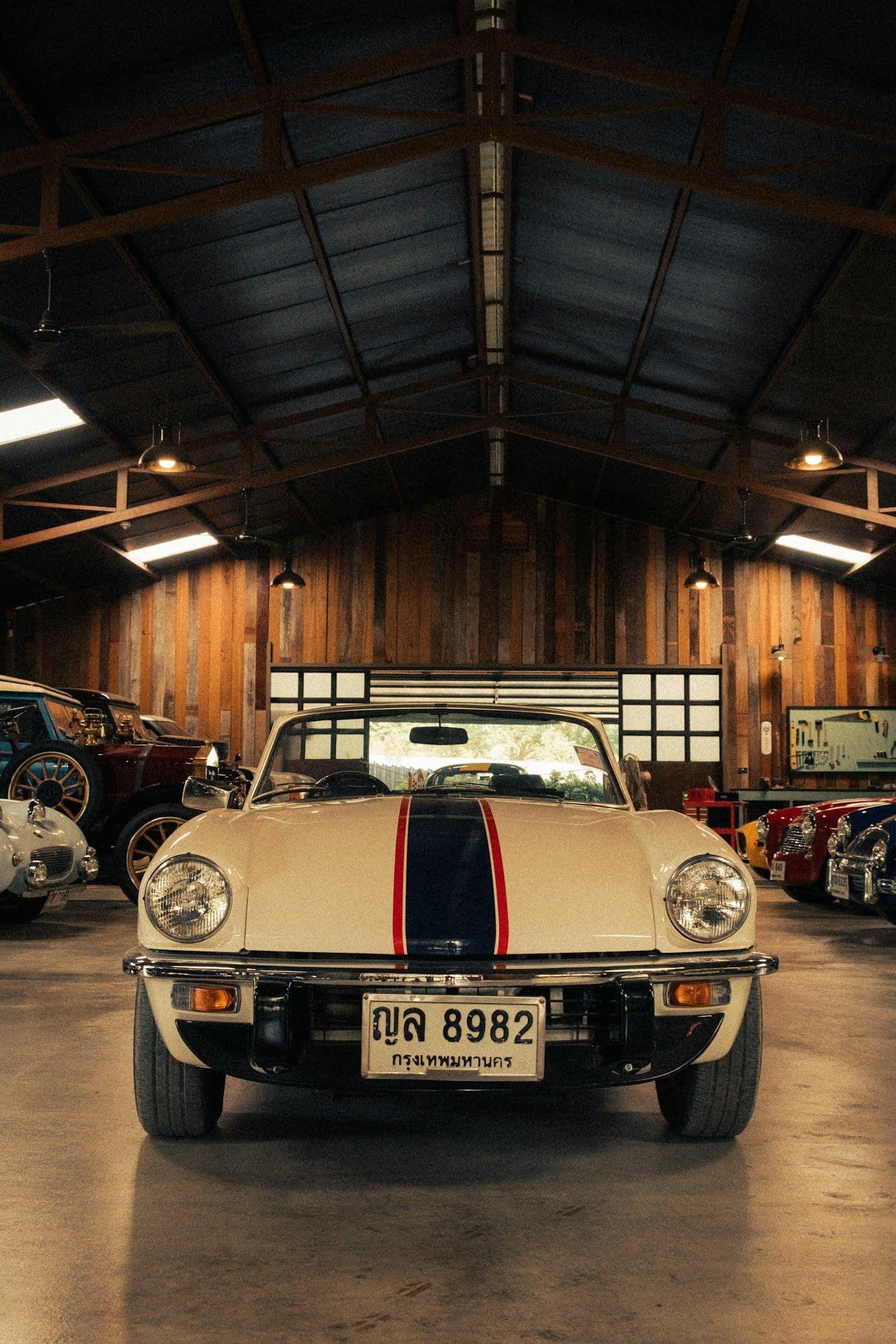 A cream roadster with a blue racing stripe on a polished concrete floor